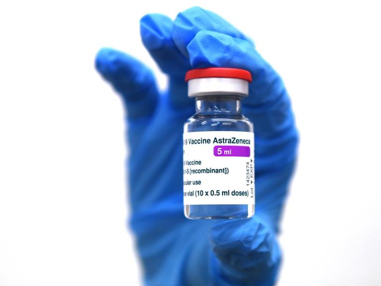 Eine Hand in blauem Schutzhandschuh hält ein Glasfläschchen mit dem Impfstoff von AstraZeneca im Lager des Universitätsklinikum in Tuebingen hohc.