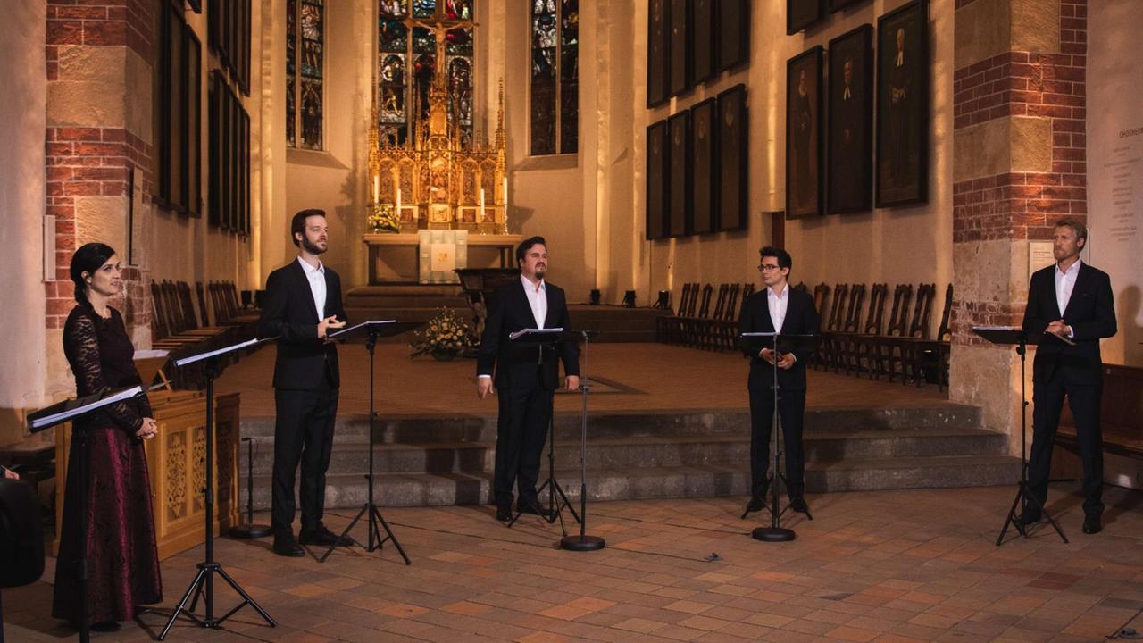 Fünf Sänger und Sängerinnen stehen im Halbrund hinter Notenständern im Kirchenraum.