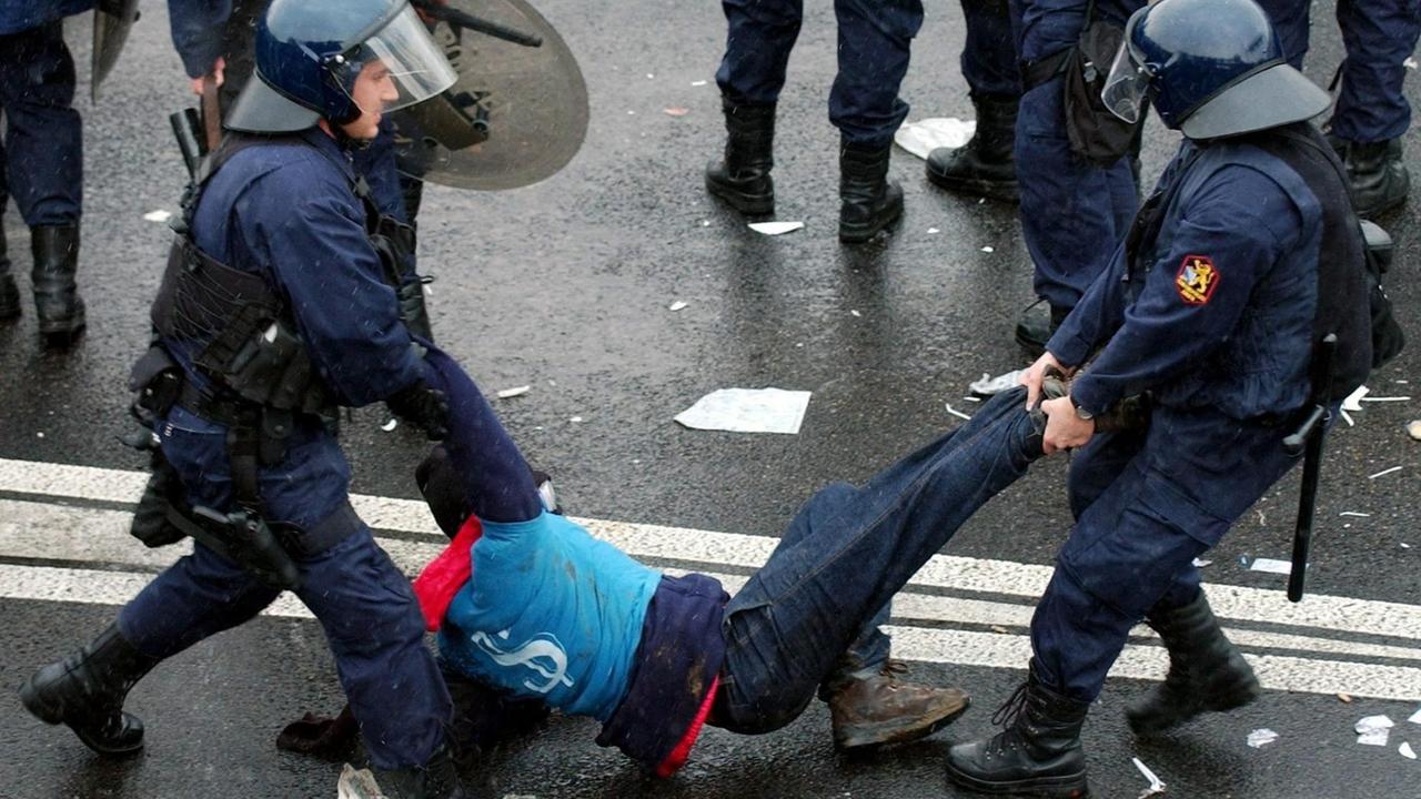 Gepanzerte Polizisten tragen einen Demonstranten von der Straße.