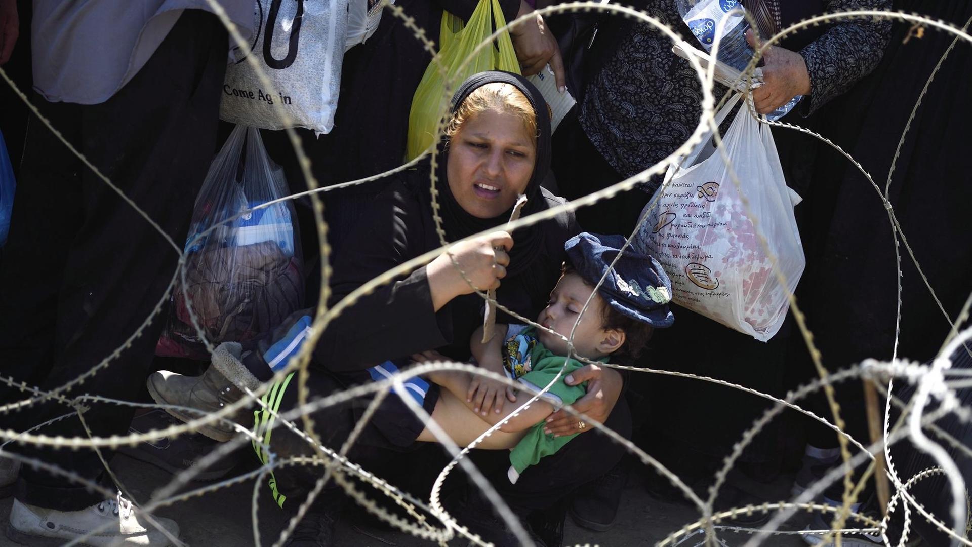 Eine Mutter kauert mit ihrem Kind vor einem Stacheldrahtzaun an der mazedonisch-griechischen Grenze
