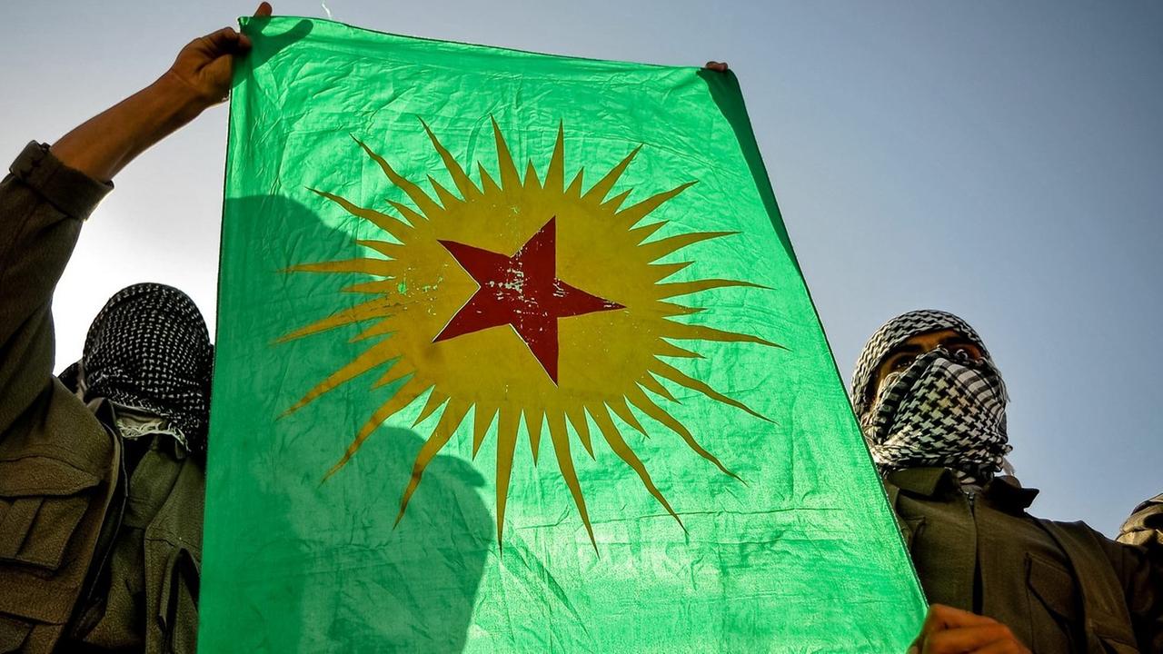 Zwei vermummte Männer halten die Fahne der verbotenen kurdischen Arbeiterpartei PKK hoch.