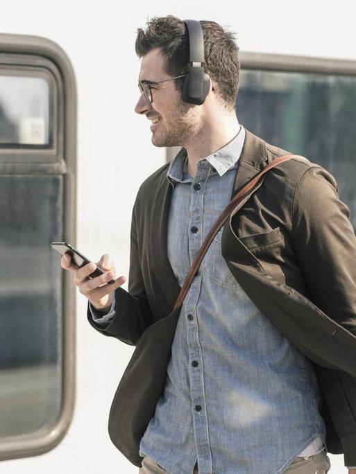 Mann mit Kopfhörern und Handy vor Zug