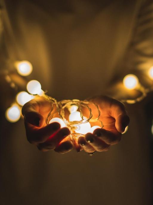 Eine Person hält die leuchtenden Lampen einer Lichterkette in den Händen.
