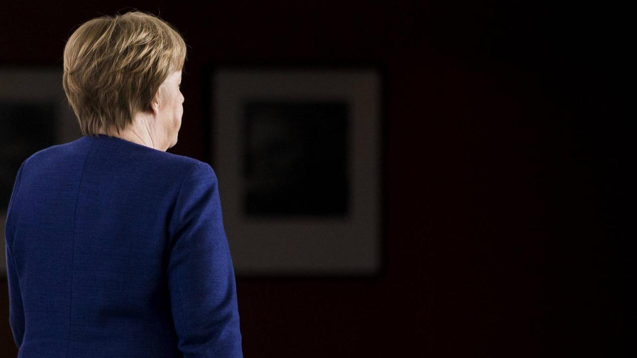 Eine Rückansicht Angela Merkels vor schwarzem Hintergrund.