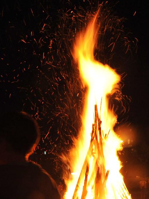 Menschen stehen nachts um ein Lagerfeuer herum.