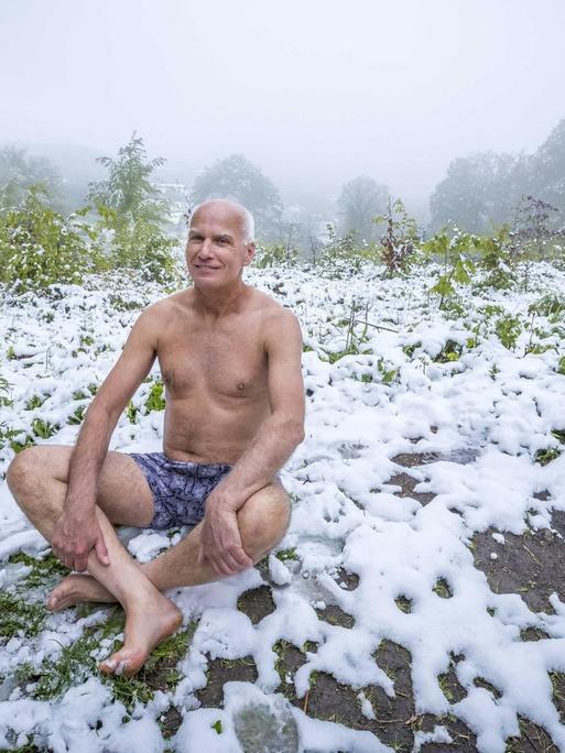 Ein Mann sitzt in Unterhose im frisch gefallenen Schnee.