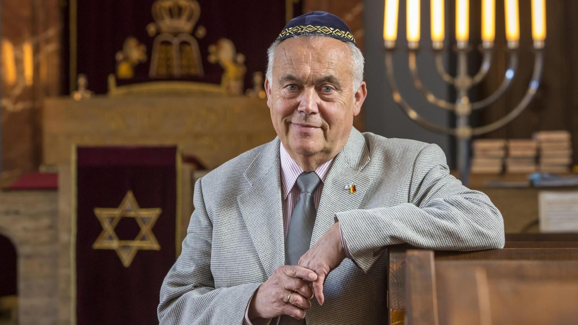 Reinhard Schramm, Vorsitzender der Jüdischen Landesgemeinde Thüringen, in einer Synagoge, in die Kamera lächelnd, den Arm auf eine Bank gestützt