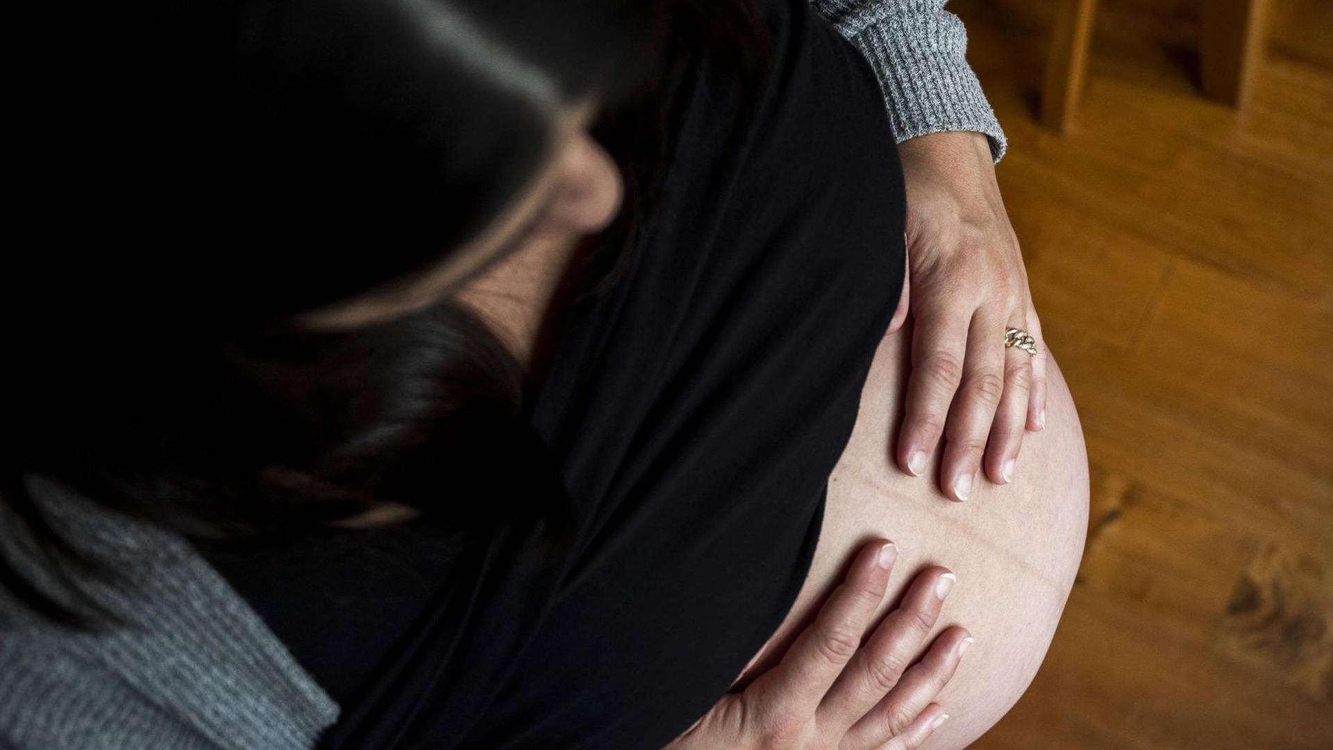 Eine Frau schaut auf ihren schwangeren Bauch hinunter.