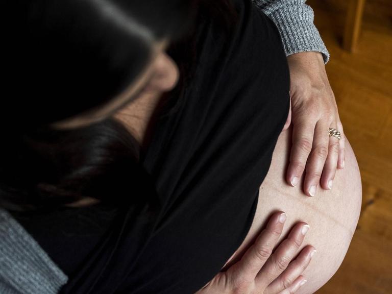 Eine Frau schaut auf ihren schwangeren Bauch hinunter.