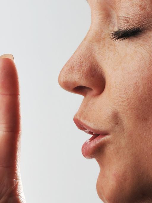 Eine Frau hält den Zeigefinger vor den Mund.