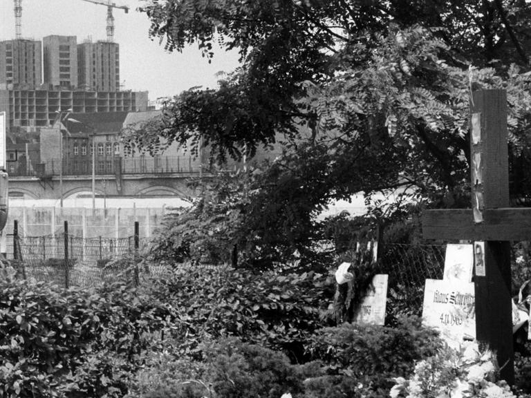 Blick von West-Berlin aus auf die Baustelle des chirurgischen Zentrums der Charité, im Bildvordergrund Gedenkkreuze für die Mauertoten.