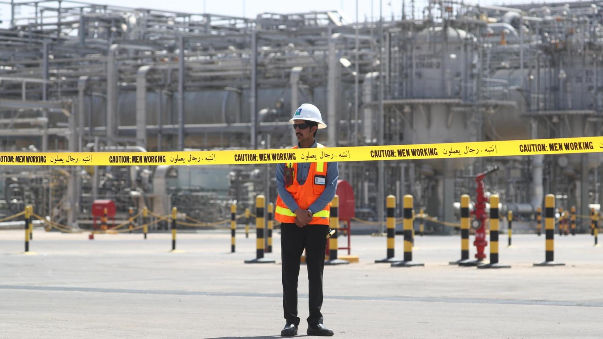 Ein Arbeiter steht vor einer Anlage des saudischen Erdölkonzerns Aramco. Vor ihm hängt ein gelbes Absperrband.