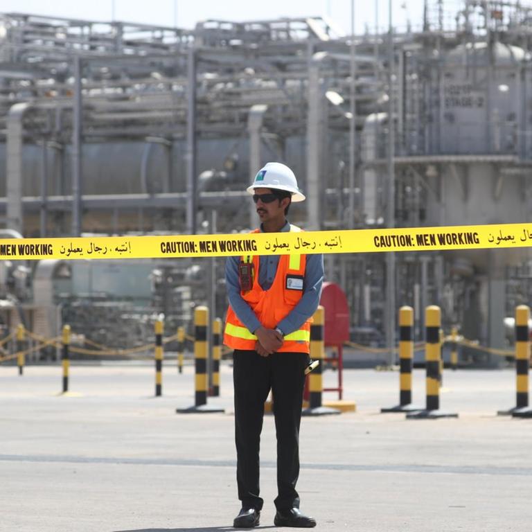 Ein Arbeiter steht vor einer Anlage des saudischen Erdölkonzerns Aramco. Vor ihm hängt ein gelbes Absperrband.
