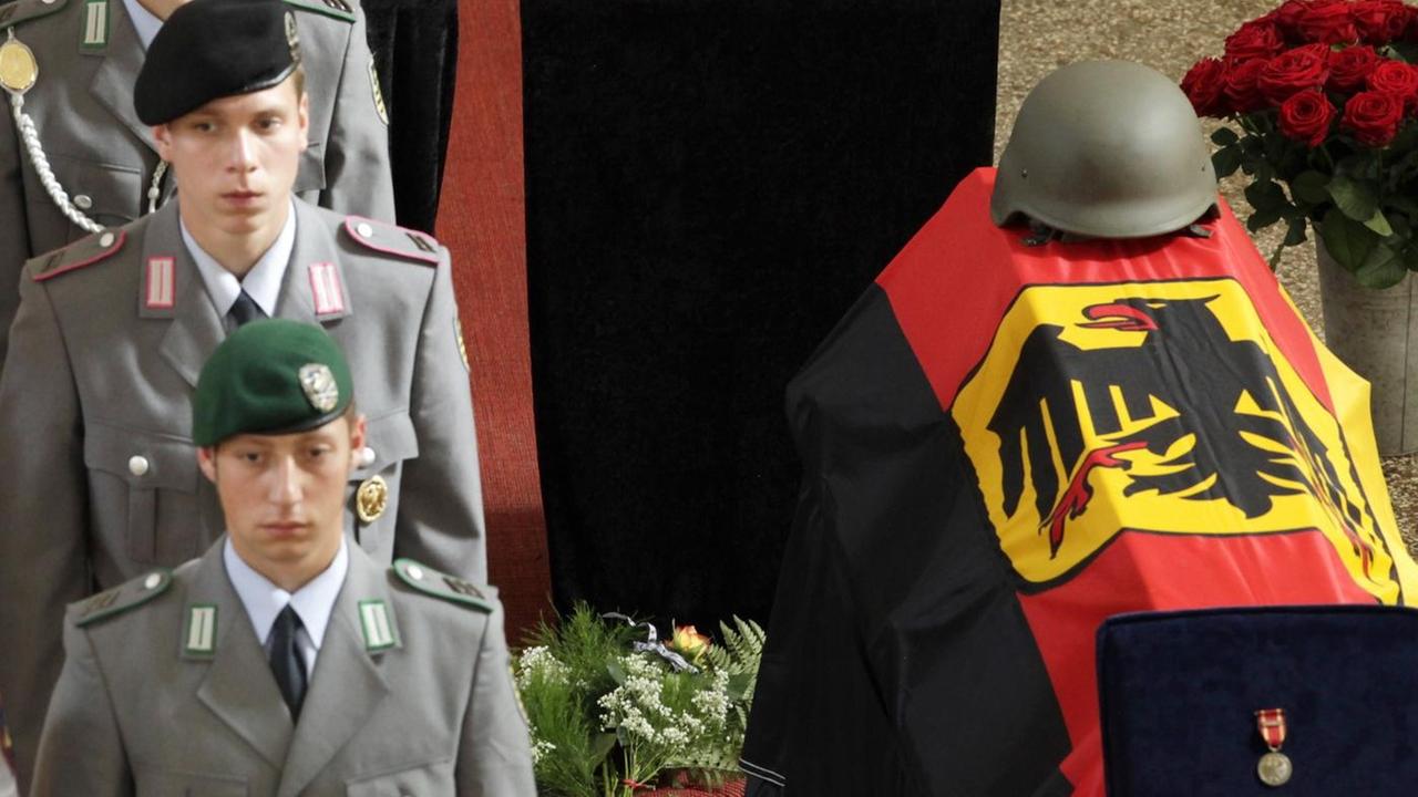 Soldaten der Bundeswehr stehen neben einem Sarg, im Hintergrund die Fotos dreier in Afghanistan getöteter Kameraden