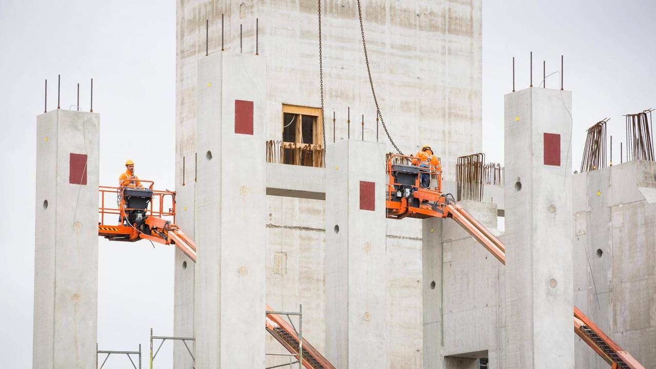 Die Bosch-Baustelle in Dresden. Zwischen grauen Betonpfeilern stehen Bauarbeiter auf orange farbenen Hebebühnen