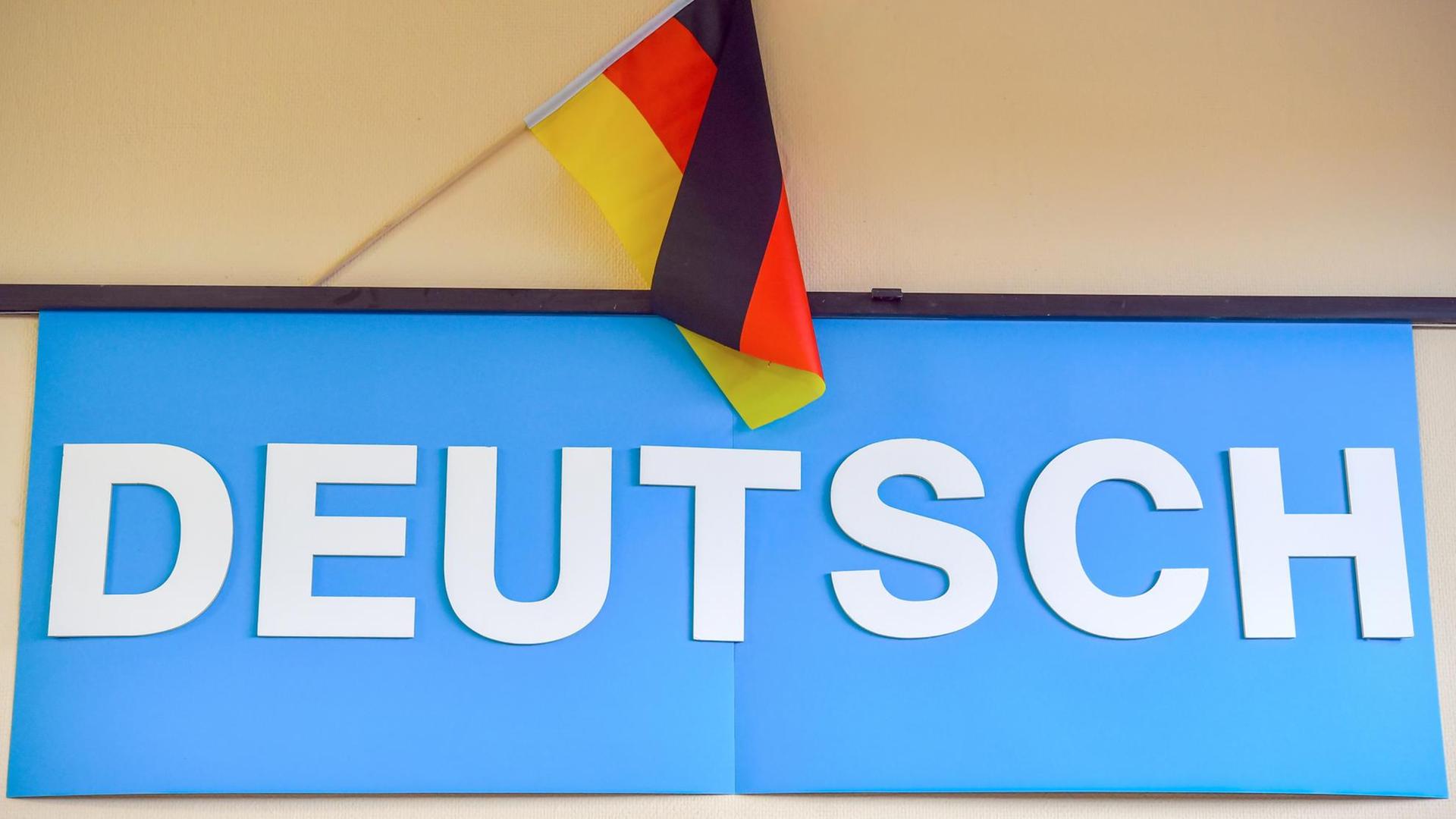 Das Foto zeigt ein blaues Plakat mit dem Text "Deutsch" in  großen Buchstaben, dahinter befindet sich eine Deutschlandfahne.