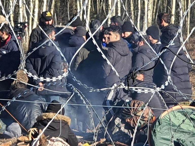 Hinter Stacheldraht ist eine Gruppe von Flüchtlingen an der polnisch-belarussischen Grenze
