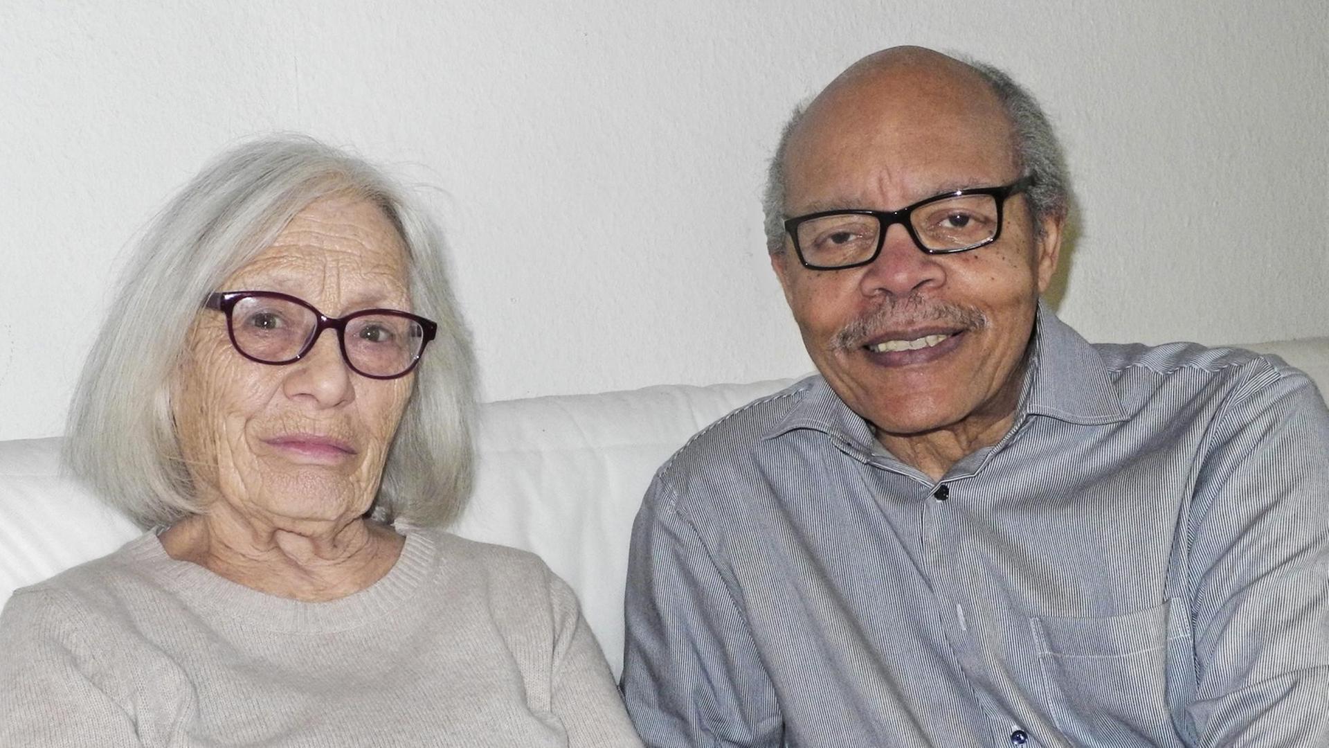 Maria und Donald Vaughn, beide um die 80 Jahre alt, sitzen auf einem Sofa und lächeln freundlich in die Kamera. Sie ist weiß, er ist schwarz. Maria und Donald Vaughn, beide um die 80 Jahre alt, sitzen auf einem Sofa und lächeln freundlich in die Kamera. Sie ist weiß, er ist schwarz.