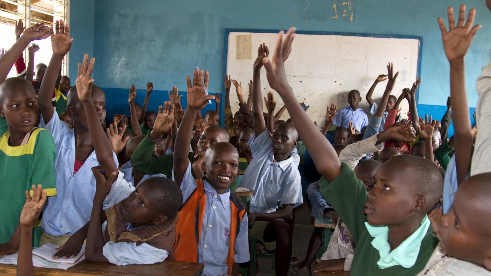Schulklasse in Kenia - viele Kinder auf engem Raum heben die Hand
