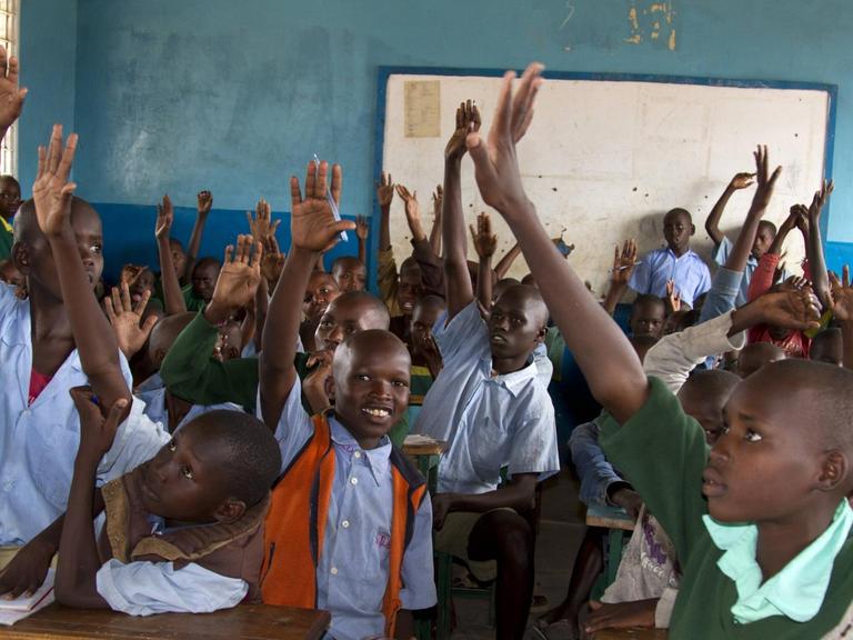 Schulklasse in Kenia - viele Kinder auf engem Raum heben die Hand