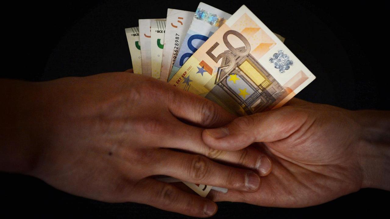 Zwei Hände. Die eine Hand gibt der andere mehrere Euroscheine.