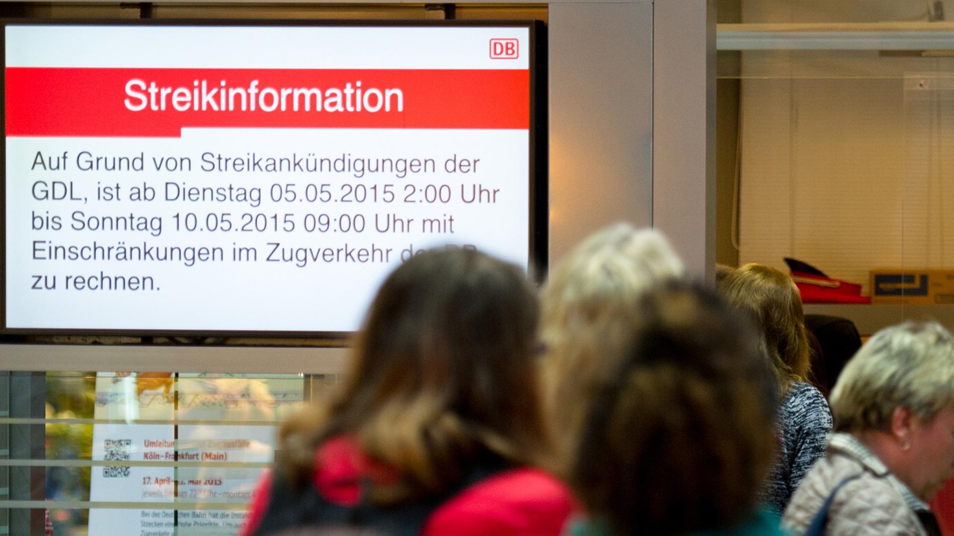 Reisende warten am 05.05.2015 an einem Informationsschalter der Deutschen Bahn auf weitere Auskünfte, während links daneben ein Bildschirm auf den aktuellen Lokführerstreik aufmerksam macht.