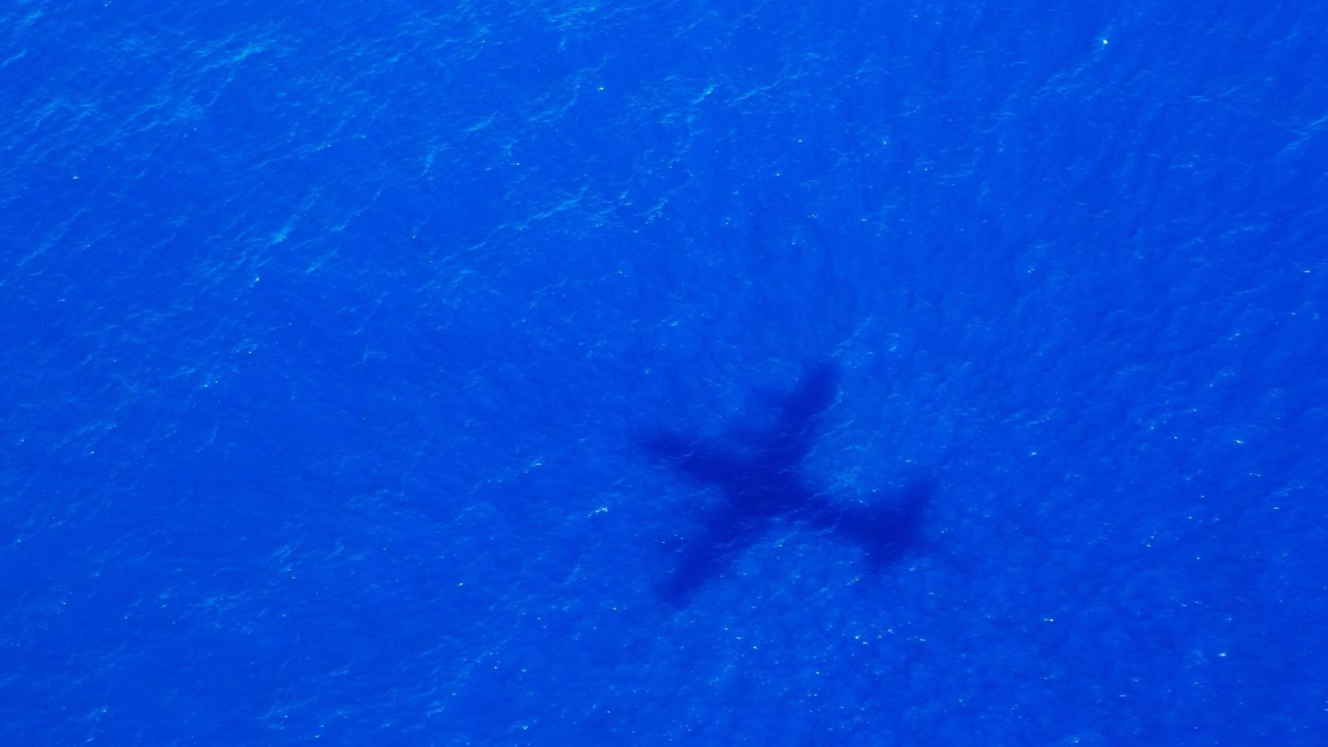 Man sieht den Schatten eines großen Flugzeuges über dem Meer