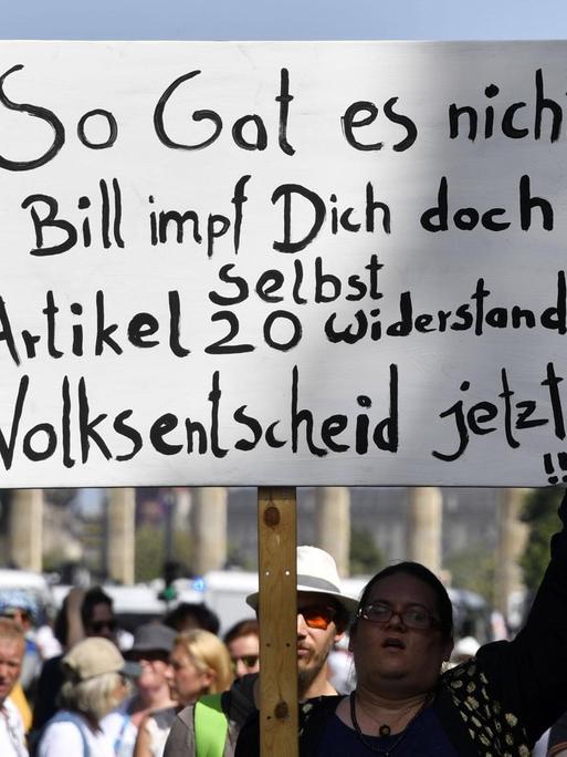 Eine Demonstrantin hält ein Schild hoch mit der Aufschrift: "So Gates nicht. Bill impf Dich doch selbst. Artikel 20. Widerstand. Volksentscheid jetzt !!!"