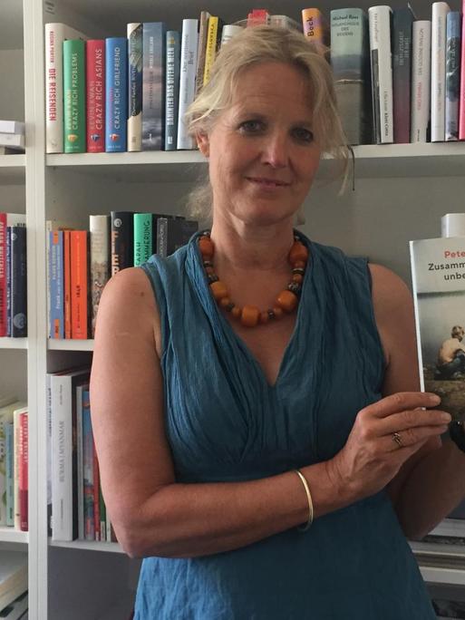Literaturredakteurin Stephanie von Oppen vor einem Bücherregal mit dem Buch von Peter Balko in der Hand.