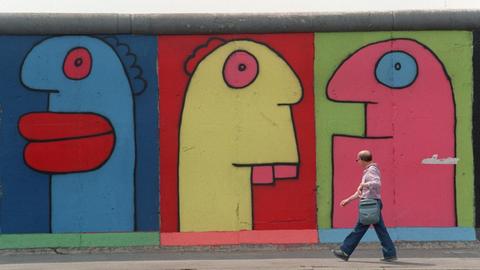 Menschen gehen im Berliner Bezirk Friedrichshain an der East Side Gallery (ehemalige Berliner Mauer) vorbei, auf denen Figuren des Künstlers Thierry Noir zu sehen sind.