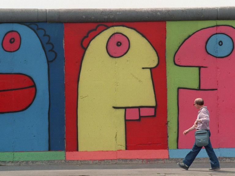 Menschen gehen im Berliner Bezirk Friedrichshain an der East Side Gallery (ehemalige Berliner Mauer) vorbei, auf denen Figuren des Künstlers Thierry Noir zu sehen sind.