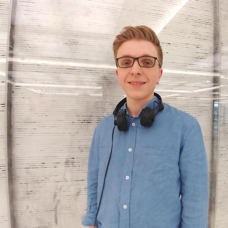 Games-Historiker Felix Zimmermann steht mit Kopfhörern vor einer gestreiften Wand im DLF