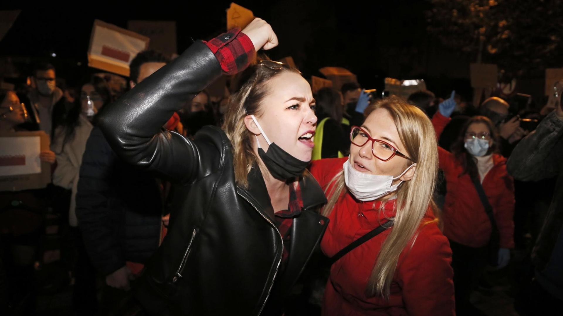 Zwei junge Frauen bei nächtlichen Protesten gegen das verschärfte Abtreibungsrecht in Polen. Eine der Frauen erhebt wütend die Faust.