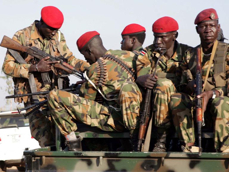 Auf einem Fahrzeug hocken fünf Regierungssoldaten in grünlichen Tarnanzügen mit roten Kappen.