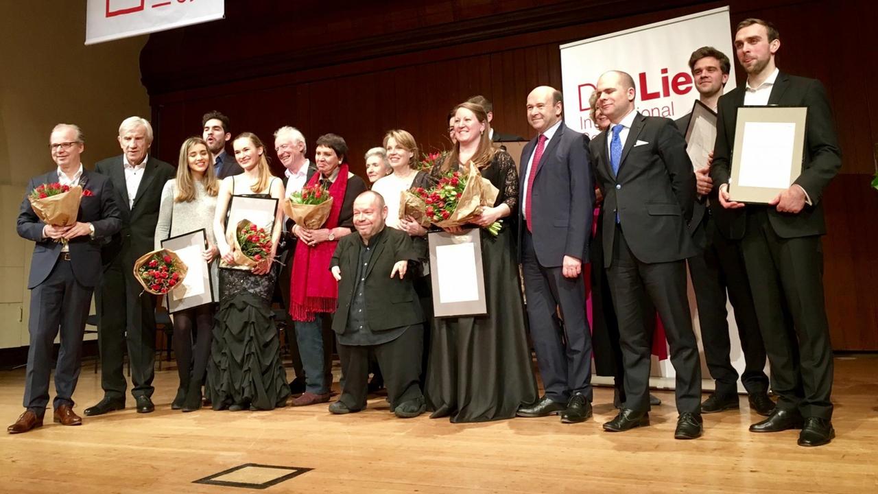 Thomas Quasthoff und die Preisträger des diesjährigen Wettbewerbs "Das Lied" stehen zum Gruppenfoto auf einer Bühne.