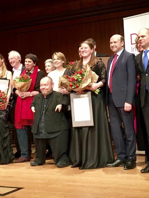 Thomas Quasthoff und die Preisträger des diesjährigen Wettbewerbs "Das Lied" stehen zum Gruppenfoto auf einer Bühne.