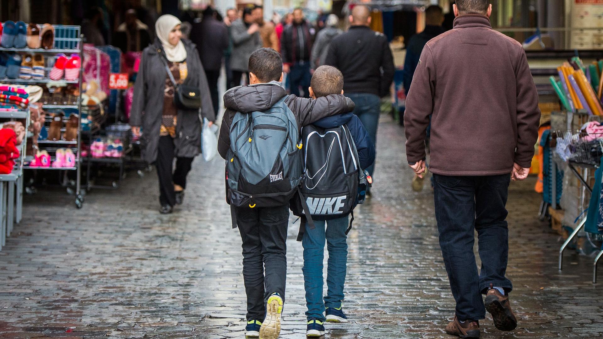 Zwei Jungen mit Rucksack laufen Arm in Arm durch eine Einkaufsstraße im Brüsseler Stadtteil Molenbeek, aufgenommen 2015