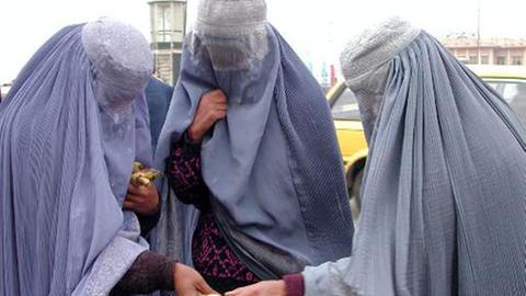 Mit Burkas bekleidete afghanische Frauen prüfen auf einem Markt in Kabul die Ware eines Bananen-Verkäufers.