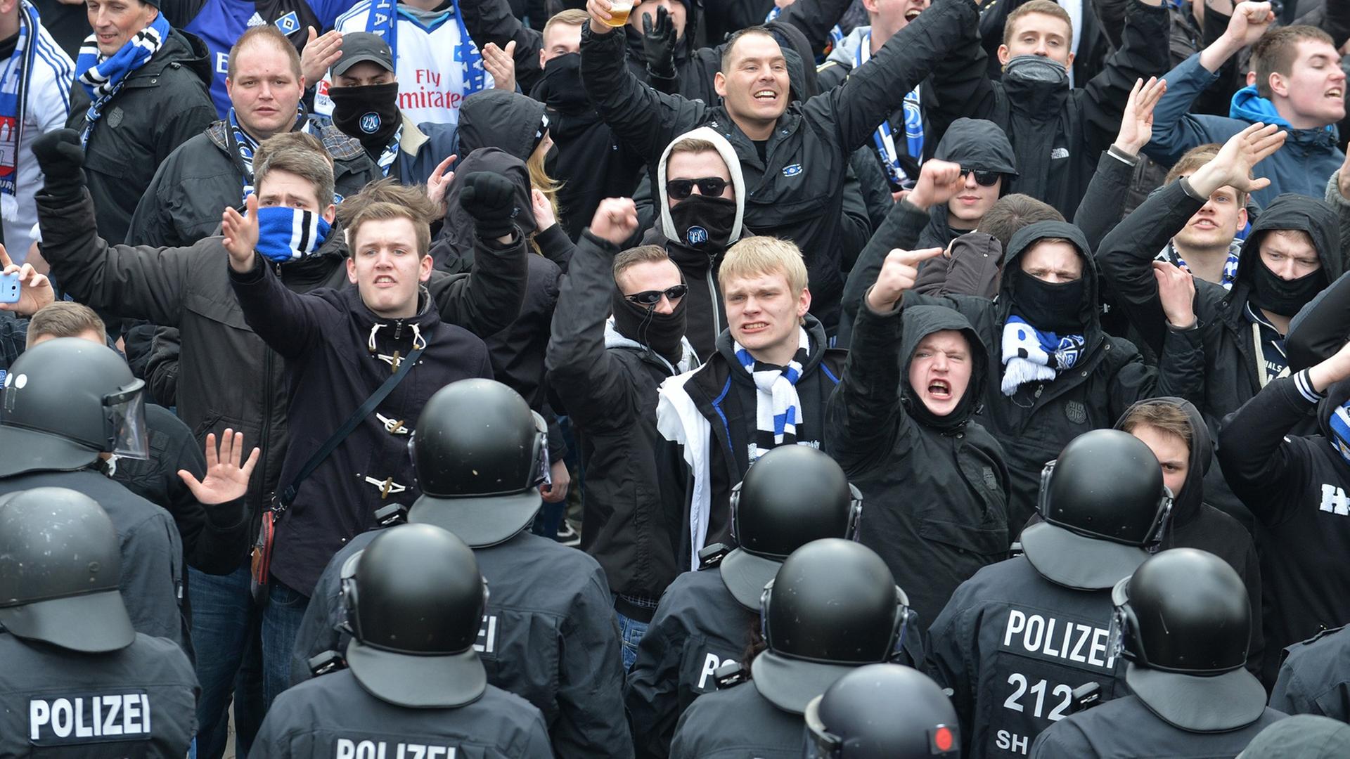 Zahlreiche Polizistinnen und Polizisten in Schutz-Kleidung und mit Helmen stehen zwischen den Fans.
