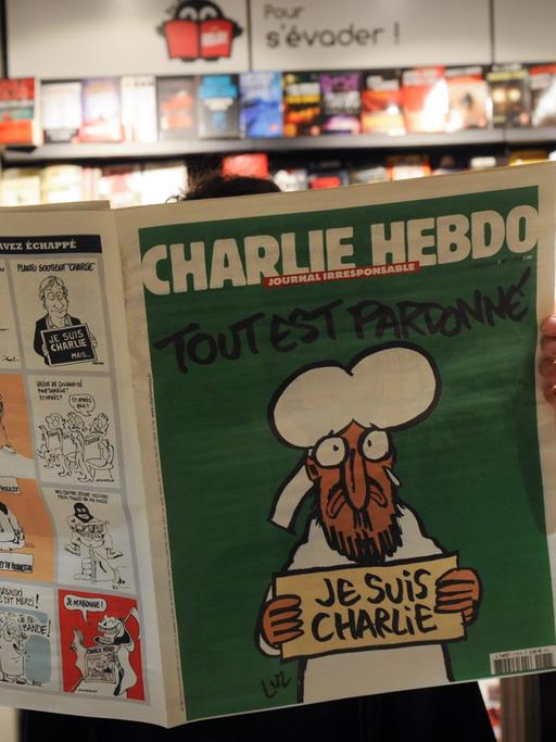 Eine Person liest in einem Pariser Kiosk die aktuelle Ausgabe der Satire-Zeitschrift "Charlie Hebdo" (14.01.2015)