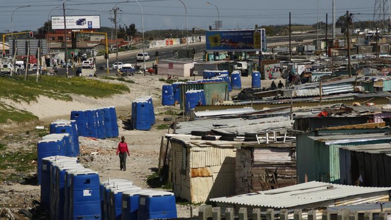 Das Bild zeigt eine südafrikanische Armensiedlung, an deren Rand eine Reihe von Toilettenhäuschen stehen