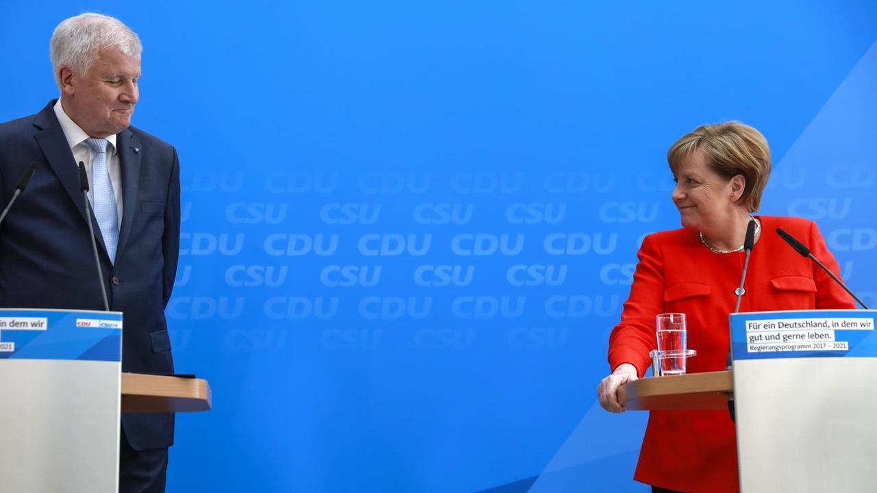 CSU-Chef Seehofer und CDU-Chefin Angela Merkel stehen an zwei Pulten nebeneinander und lächeln sich an.