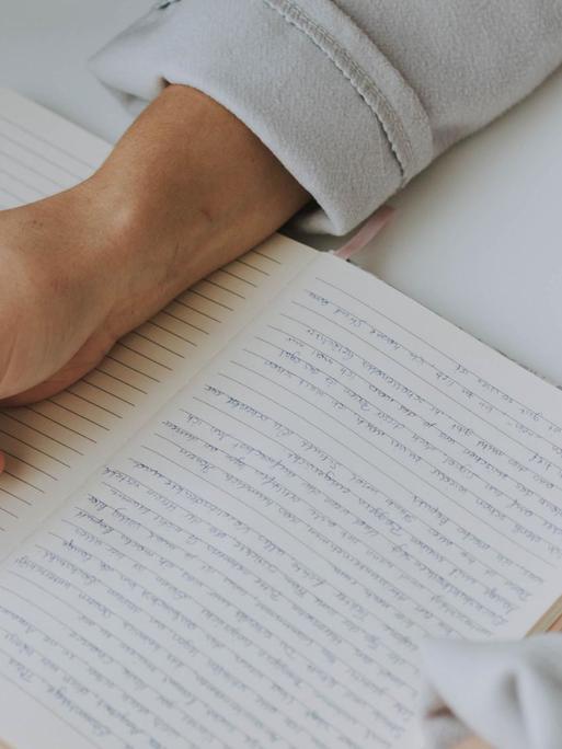 Eine Person schreibt mit einem Kugelschreiber in einem linierten Buch