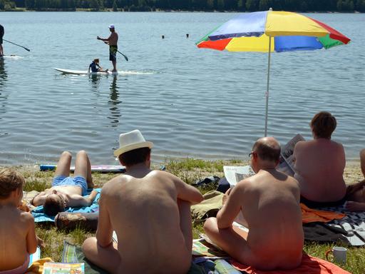 Am Moritzsee bei Leipzig (Sachsen) sitzen Badegäste bei über 30 Grad Hitze an einem FKK-Abschnitt und beobachten zwei vorbeifahrende Stehpaddler auf dem Wasser, aufgenommen am 08.06.2014.