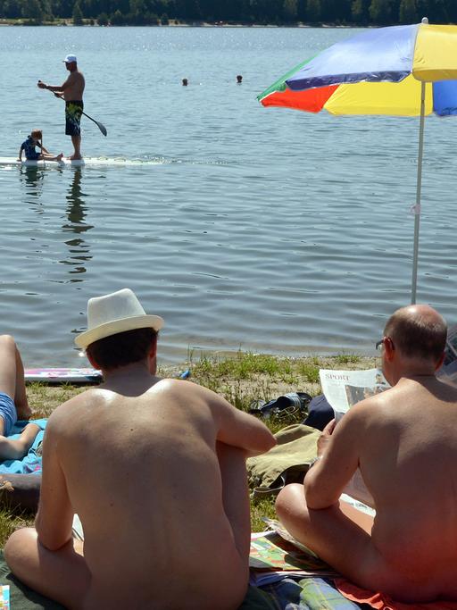 Am Moritzsee bei Leipzig (Sachsen) sitzen Badegäste bei über 30 Grad Hitze an einem FKK-Abschnitt und beobachten zwei vorbeifahrende Stehpaddler auf dem Wasser, aufgenommen am 08.06.2014.