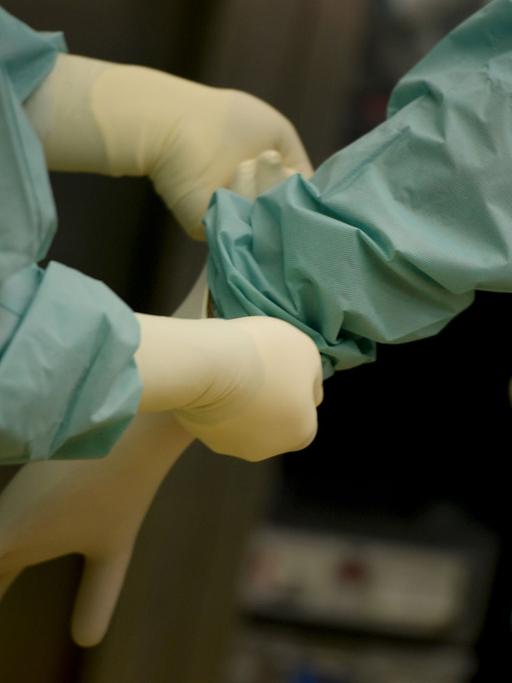 Ein Mediziner bekommt am 18.02.2014 in einer Klinik in Baden-Württemberg vor einer Operation ein Paar Handschuhe angezogen.