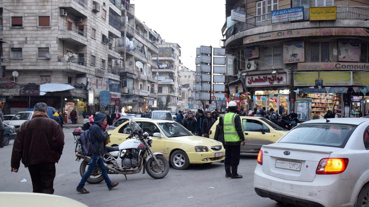 Sie sehen Menschen, Autos und einen Verkehrs-Polizisten an einer Straßen-Kreuzung in Aleppo.