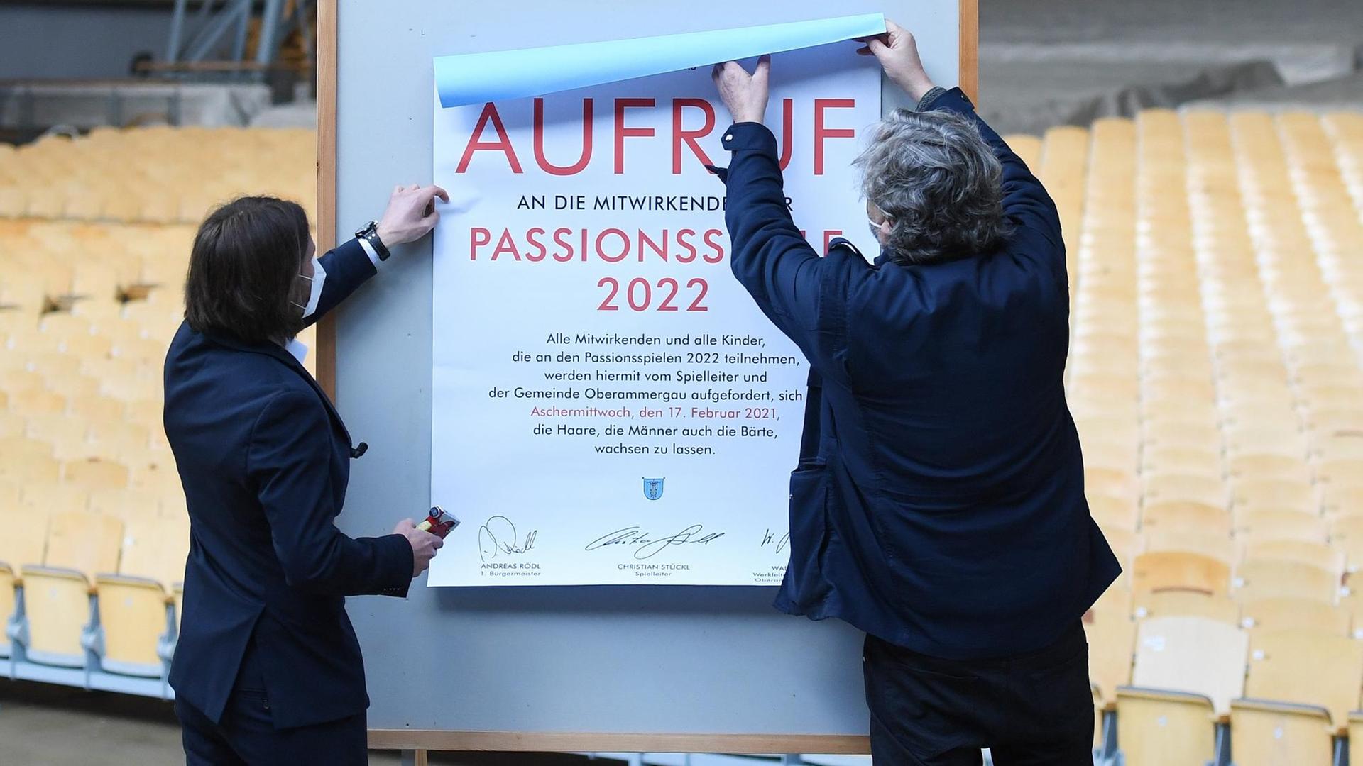 Der Spielleiter der Passionsspiele Christian Stückl (rechts) und der Bürgermeister von Oberammergau Andreas Rödl bringen das Plakat zum "Haar -und Barterlass" für die wegen Corona auf 2022 verschobenen Passionsspiele an.