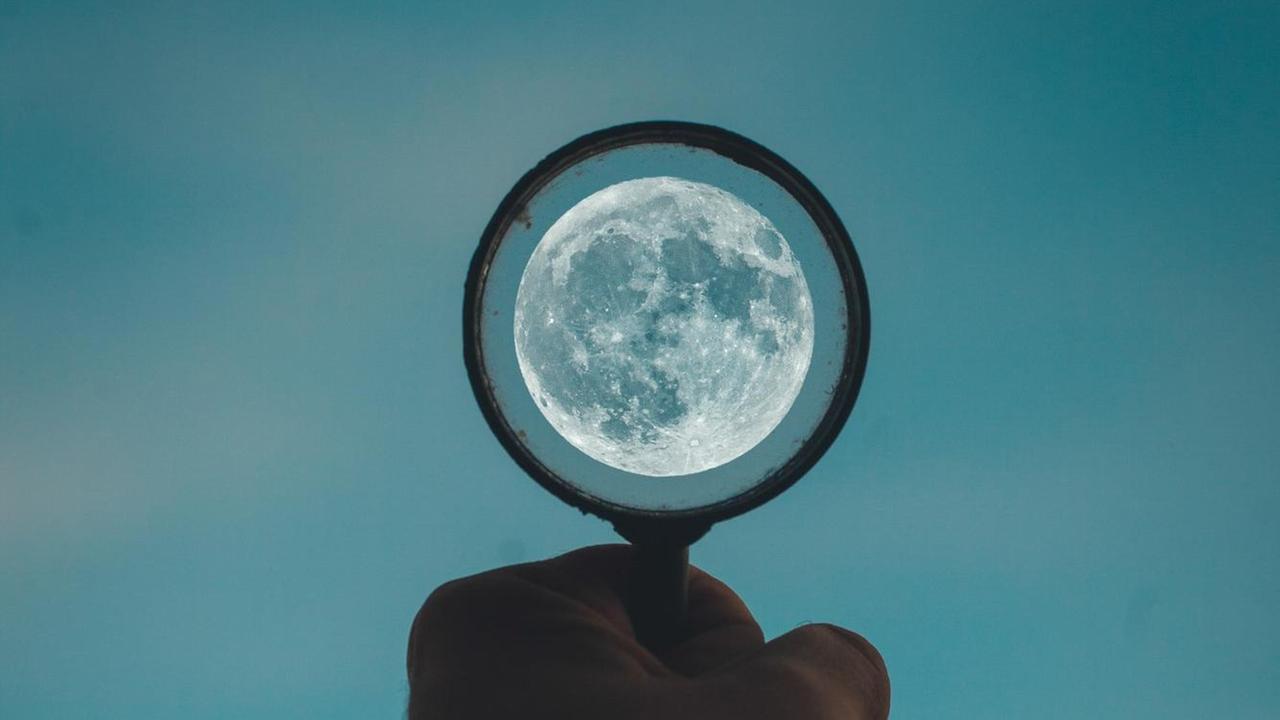 Eine Hand hält einen Kreis gen Abendhimmel, in deren Mitte der Mond leuchtet.