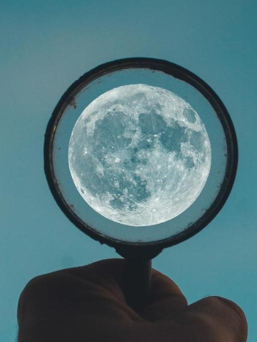 Eine Hand hält einen Kreis gen Abendhimmel, in deren Mitte der Mond leuchtet.